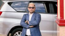 Praktisi hukum berdiri percaya diri mengenakan jas biru di depan mobil