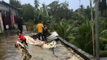 Warga membersihkan reruntuhan atap dan jalan retak akibat pergeseran tanah di Aceh Tamiang, sementara seorang anak bermain di sekitar lokasi.